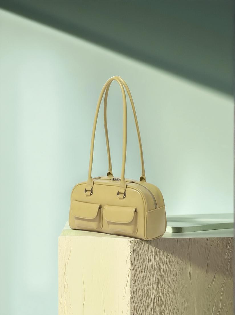 A Beige Handbag Is Elegantly Displayed On A Textured Pedestal In A Softly Lit Minimalist Setting