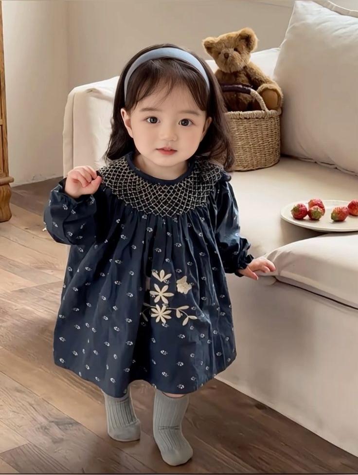 A Little Girl In A Navy Blue Dress Stands In A Cozy Living Room With A Teddy Bear And Strawberries On A Nearby Couch