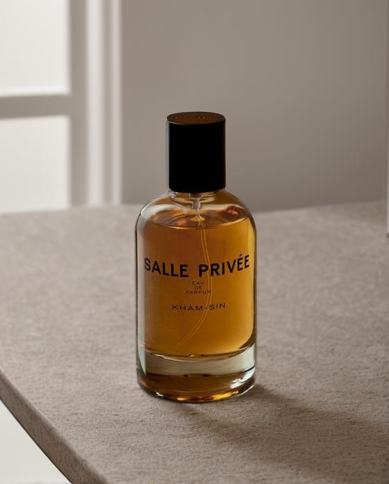 A Bottle Of Salle Privée Perfume Rests Elegantly On A Minimalist Countertop In A Softly Lit Room