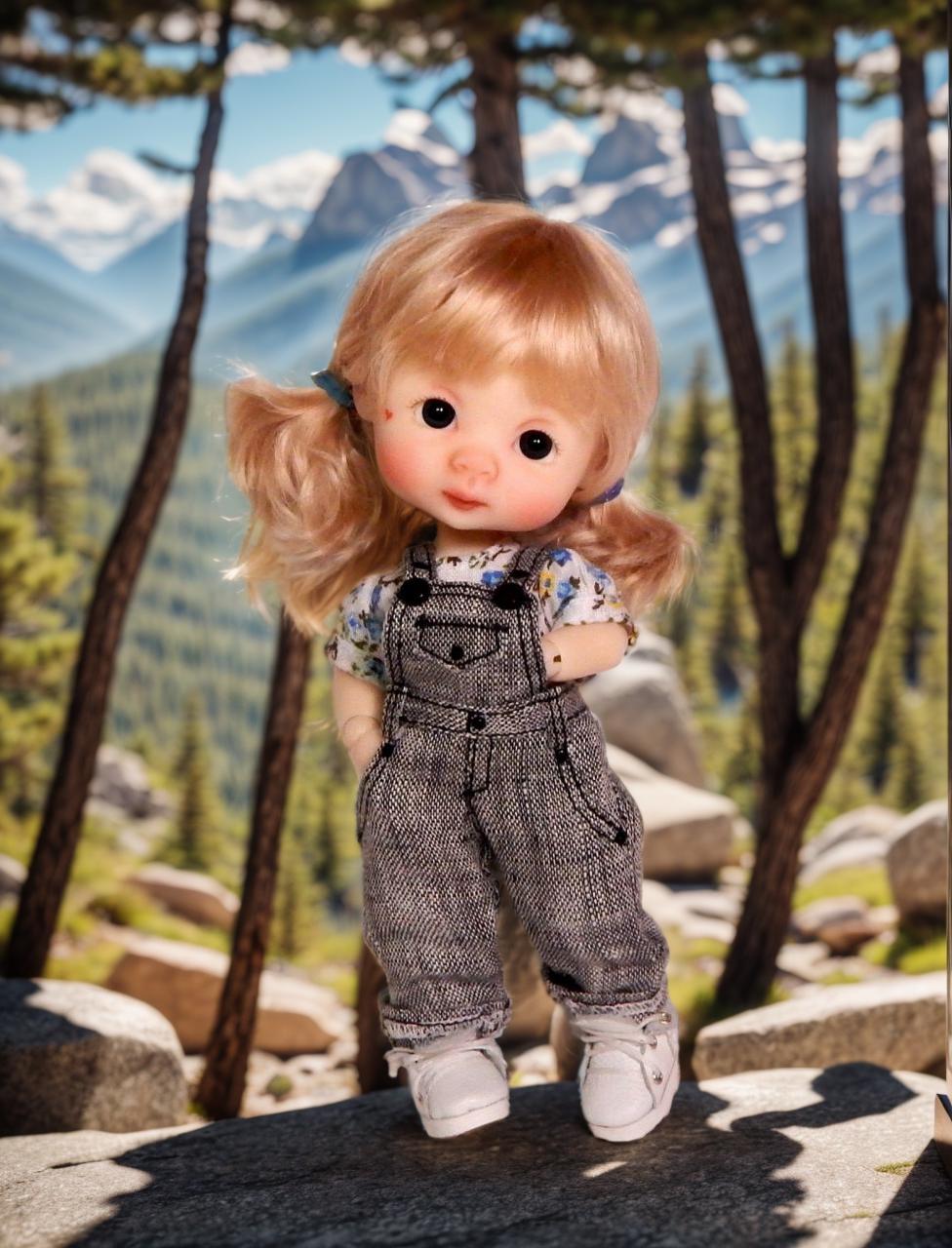 A Doll With Blonde Hair Is Dressed In Overalls And Standing In A Scenic Mountain Landscape