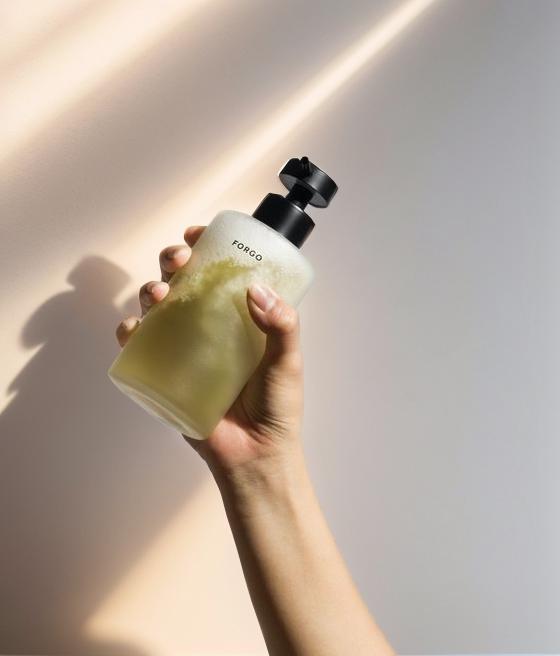 A Hand Holding A Clear Frosted Bottle Of Liquid Soap In Front Of A Softly Lit Background
