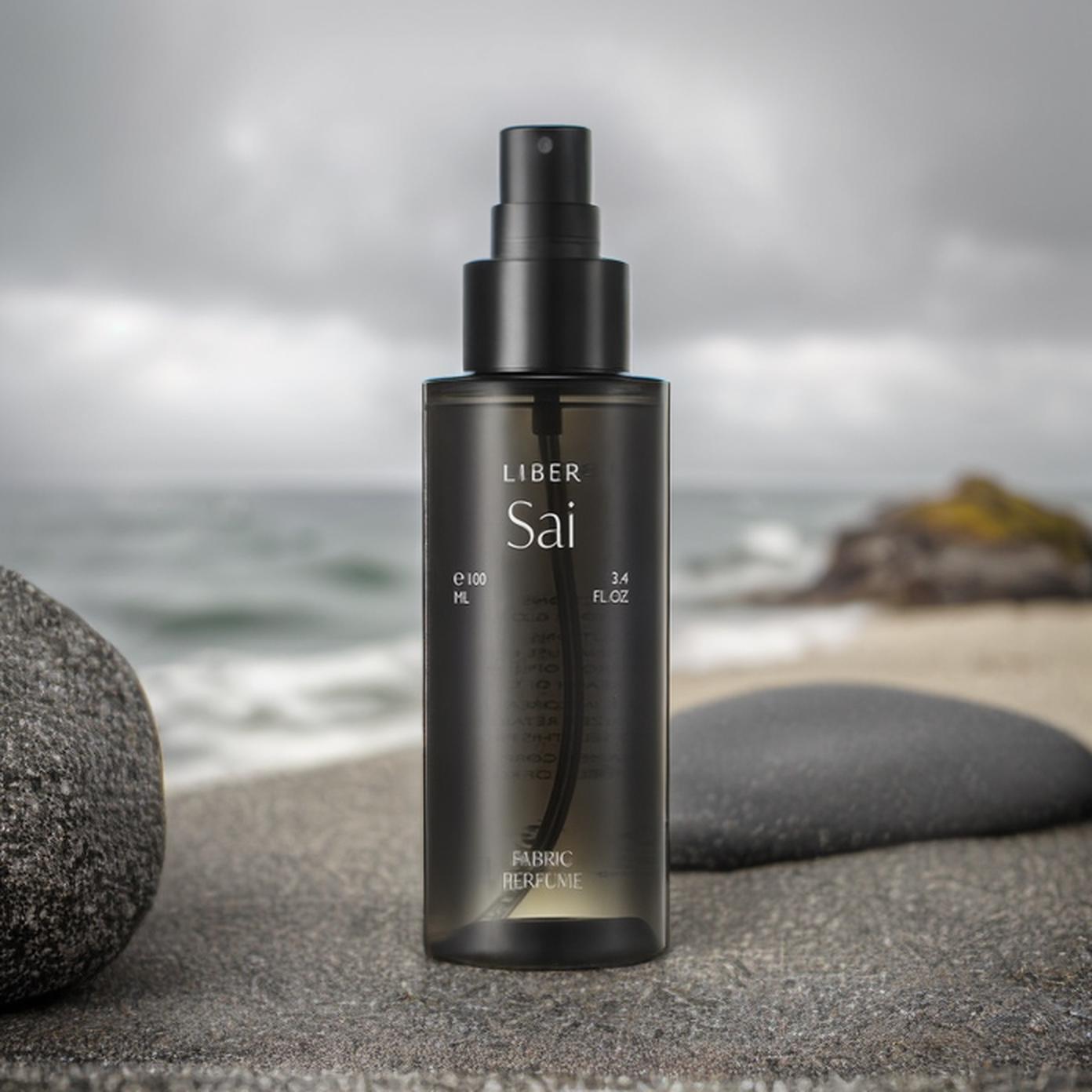A Sleek Bottle Of Liber Sai Fabric Perfume Is Elegantly Displayed On A Rocky Beach With The Ocean In The Background