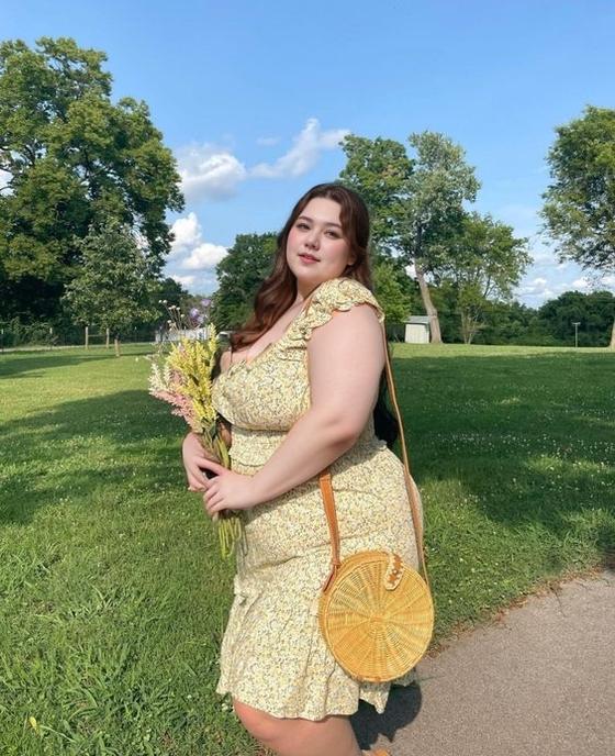 A Woman In A Floral Dress Holds A Bouquet Of Flowers While Standing In A Sunny Park