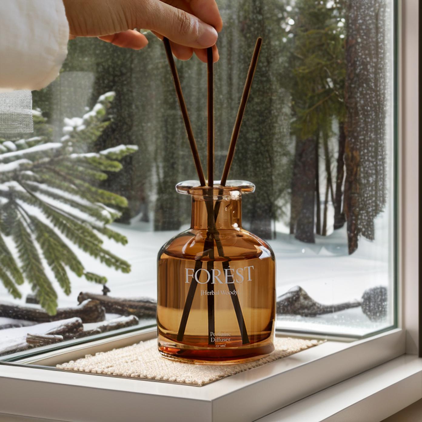 A Hand Places Diffuser Sticks Into A Jar Labeled "Forest" By A Snowy Window Creating A Cozy And Aromatic Atmosphere