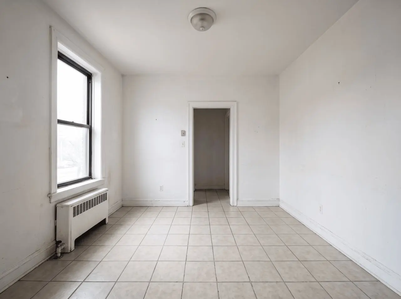 Synthetic empty apartment living room with beige tile, one black-framed window, a radiator, and a centered back doorway