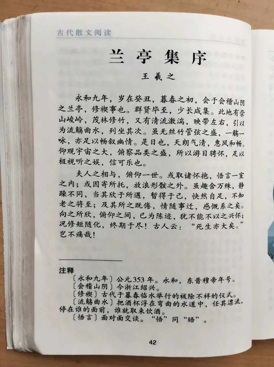 An open Chinese textbook page combines the title, main text, annotations, and a desk setting.